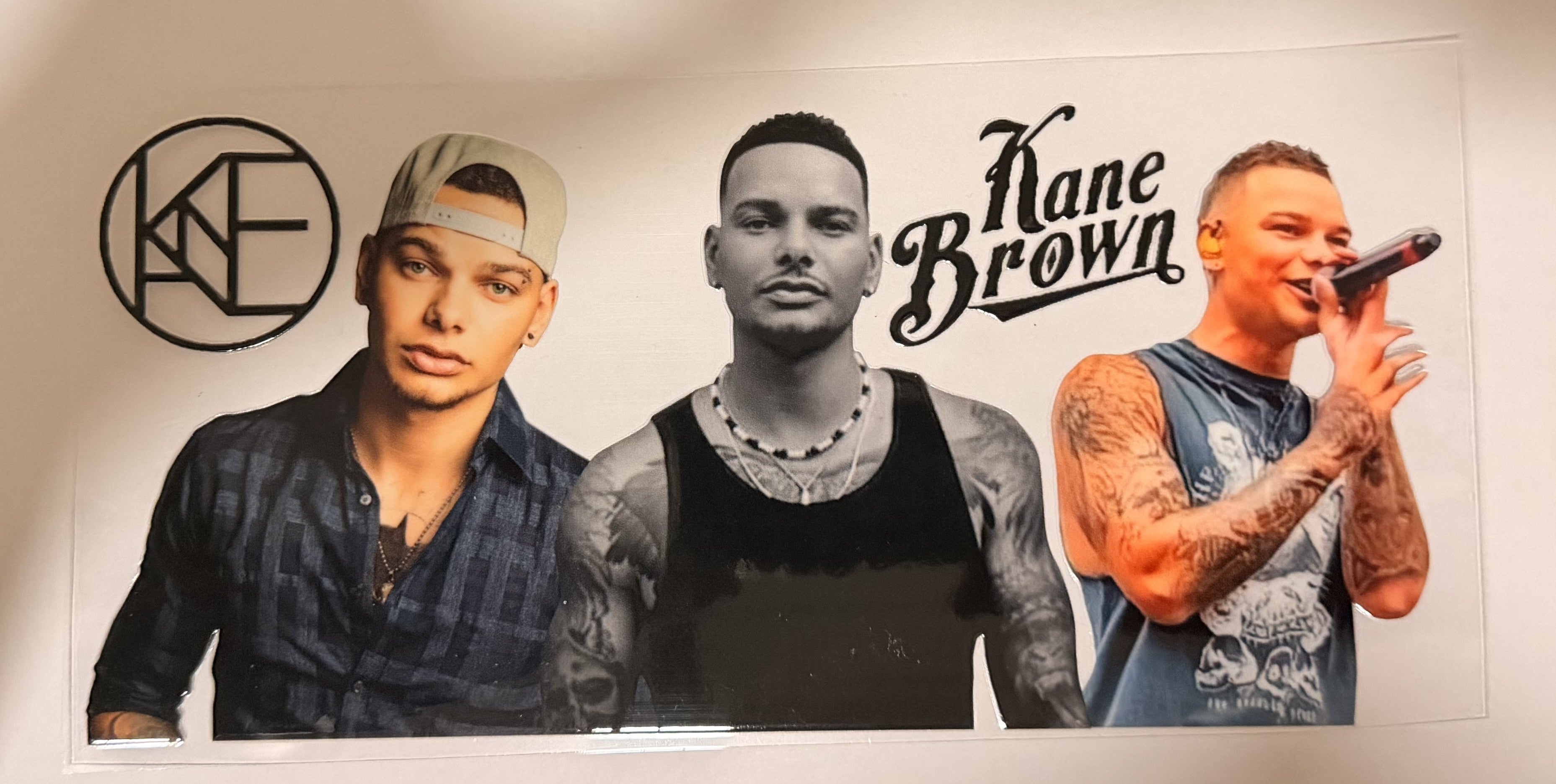 A large wall decal or poster featuring three portraits of rapper Kane Brown, including a black-and-white center portrait, a color portrait on the left, and a color portrait on the right with a microphone, plus the text 'Kane Brown' and a circular 'KF' logo.