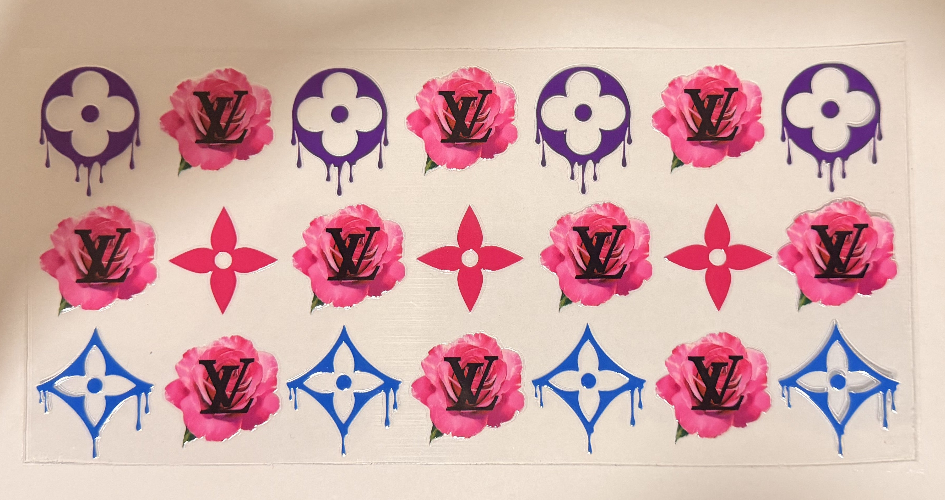 A sheet of Louis Vuitton-inspired monogram and floral decals, featuring pink roses with black LV logos, purple and blue monogram motifs, and dripping paint effects, arranged on a white background.