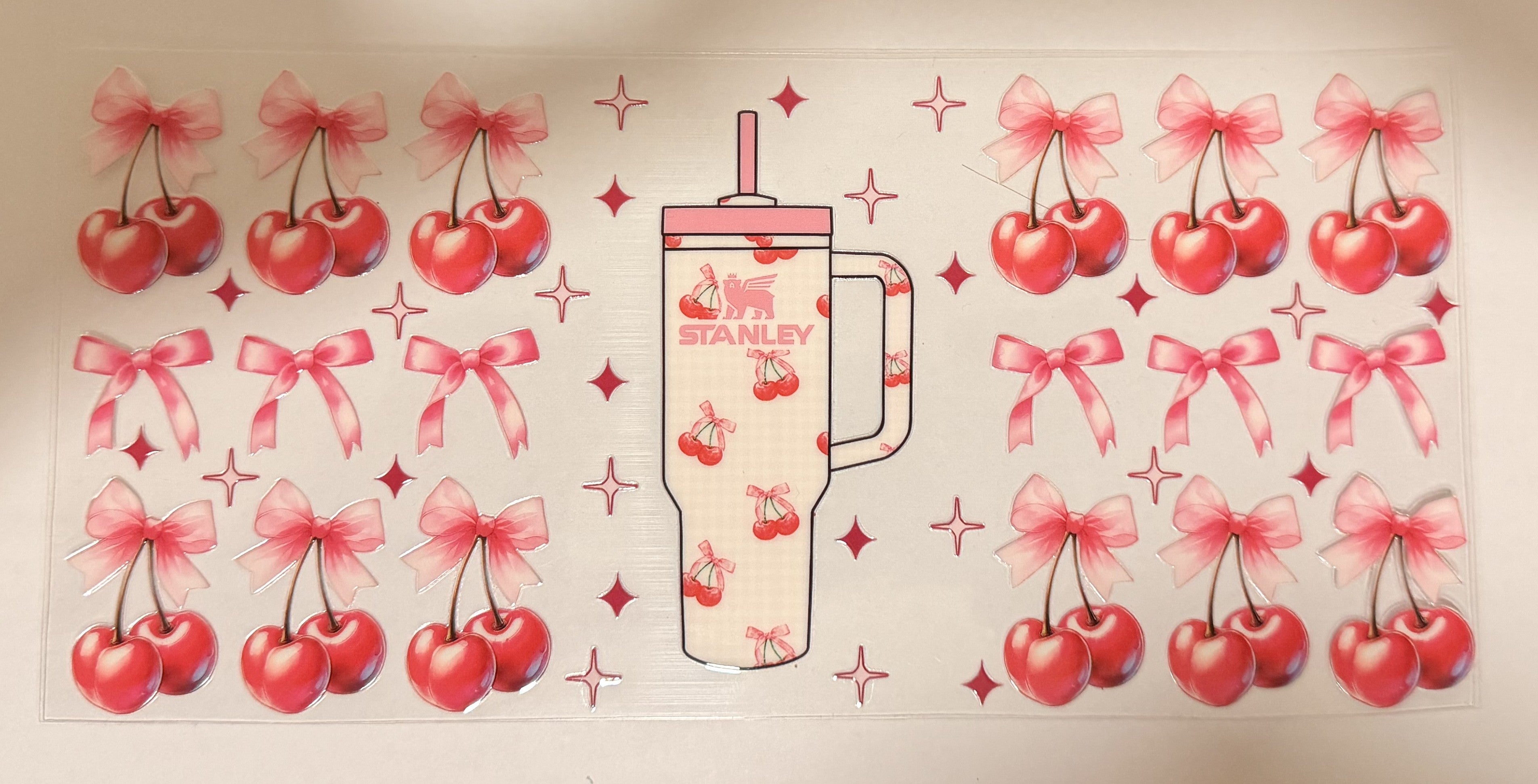 A sheet of decorative decals featuring a central Stanley tumbler illustration surrounded by repeated cherries with pink bows and small star accents on a white background.