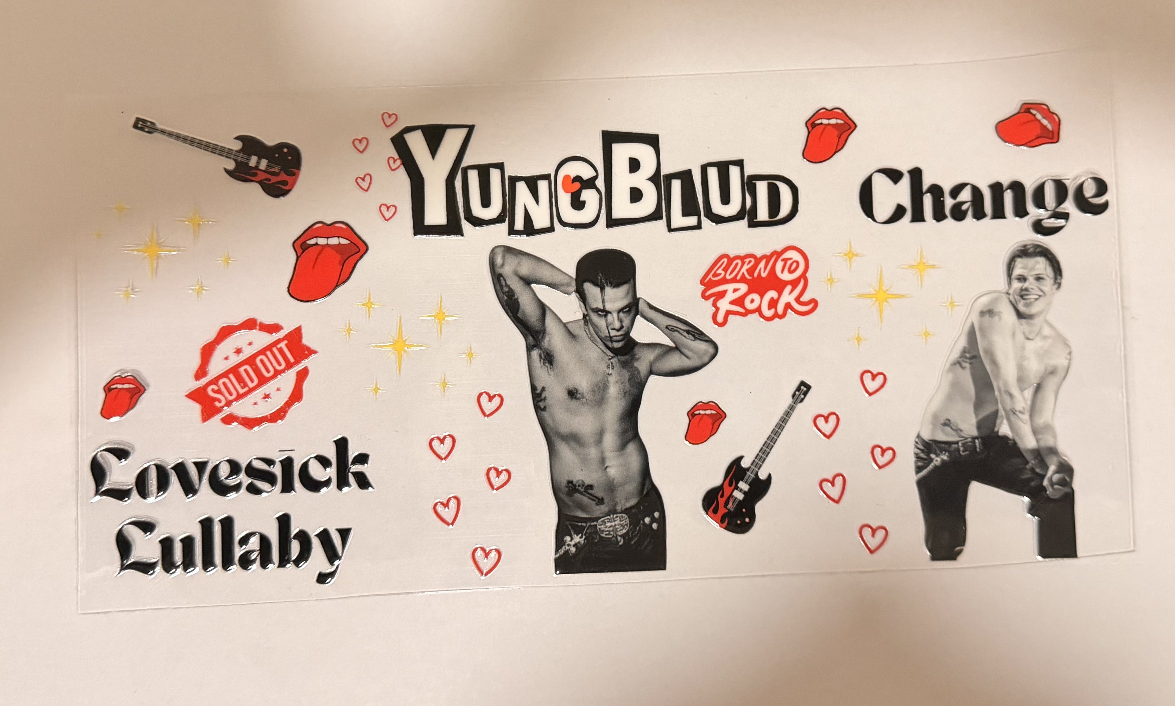 A rectangular printed poster or sticker featuring stylized text and illustrated figures. The design includes the words 'YungBlud', 'Change', 'Coversick Lullaby', 'Born to Rock', and 'Sold Out' with red lips, hearts, stars, and guitar illustrations on a white background.