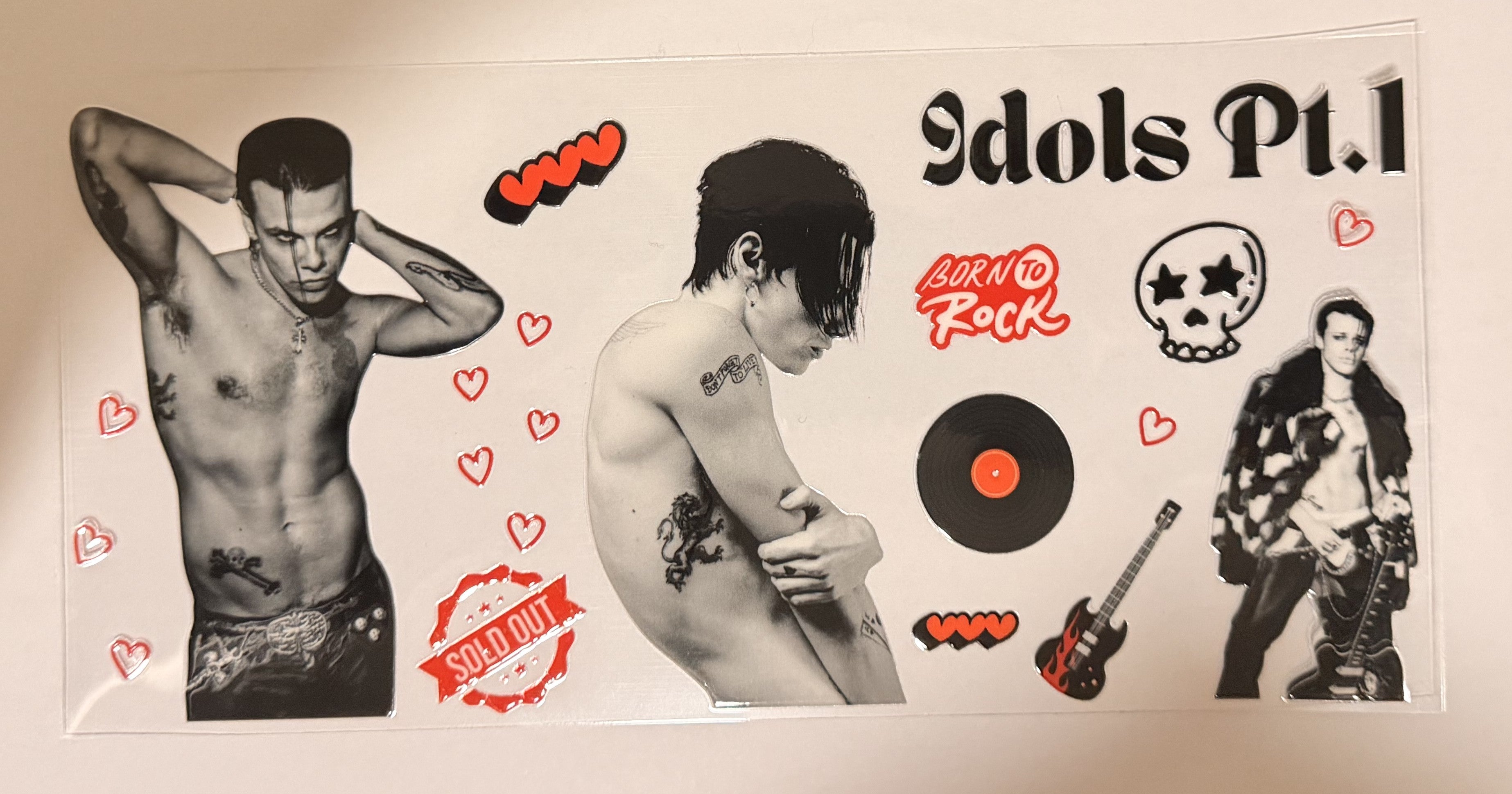 A rectangular printed sticker or decal sheet featuring three shirtless male models, black-and-white portraits, red hearts, a vinyl record, a guitar, a skull with star eyes, and the text 'Idols Pt.1' and 'Born to Rock'.