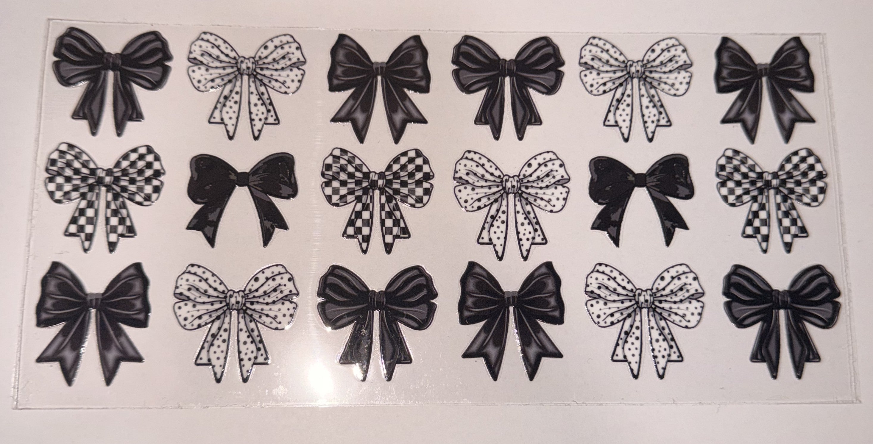 A sheet of clear nail wraps or decals featuring 16 different bow designs in black and white patterns, including solid black, checkered, and polka dot bows, displayed on a white background.