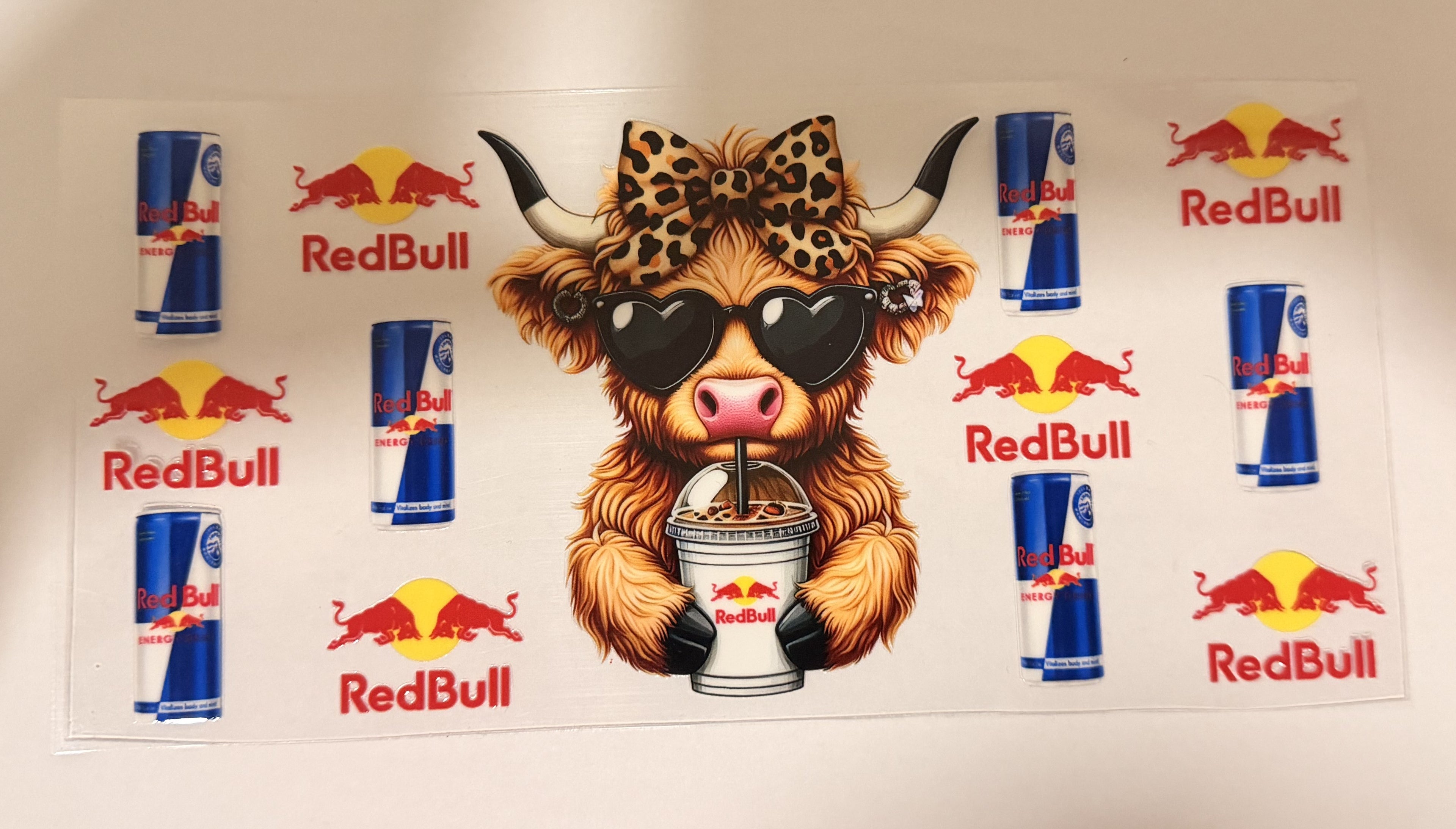 A Red Bull themed sticker sheet featuring a central cartoon highland cow wearing a leopard-print bow and black sunglasses, holding a Red Bull can. The sheet is surrounded by multiple smaller Red Bull can illustrations and logos on a white background.